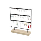 Black metal earring holder with three rows on a natural wood base displayed with assorted earrings.