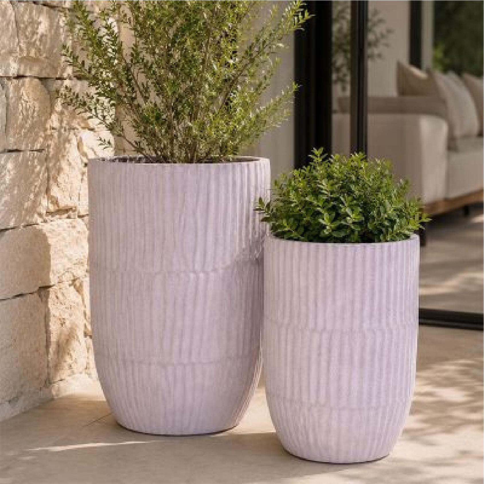 Two tall, ribbed grey ceramic planter pot with plants on a patio