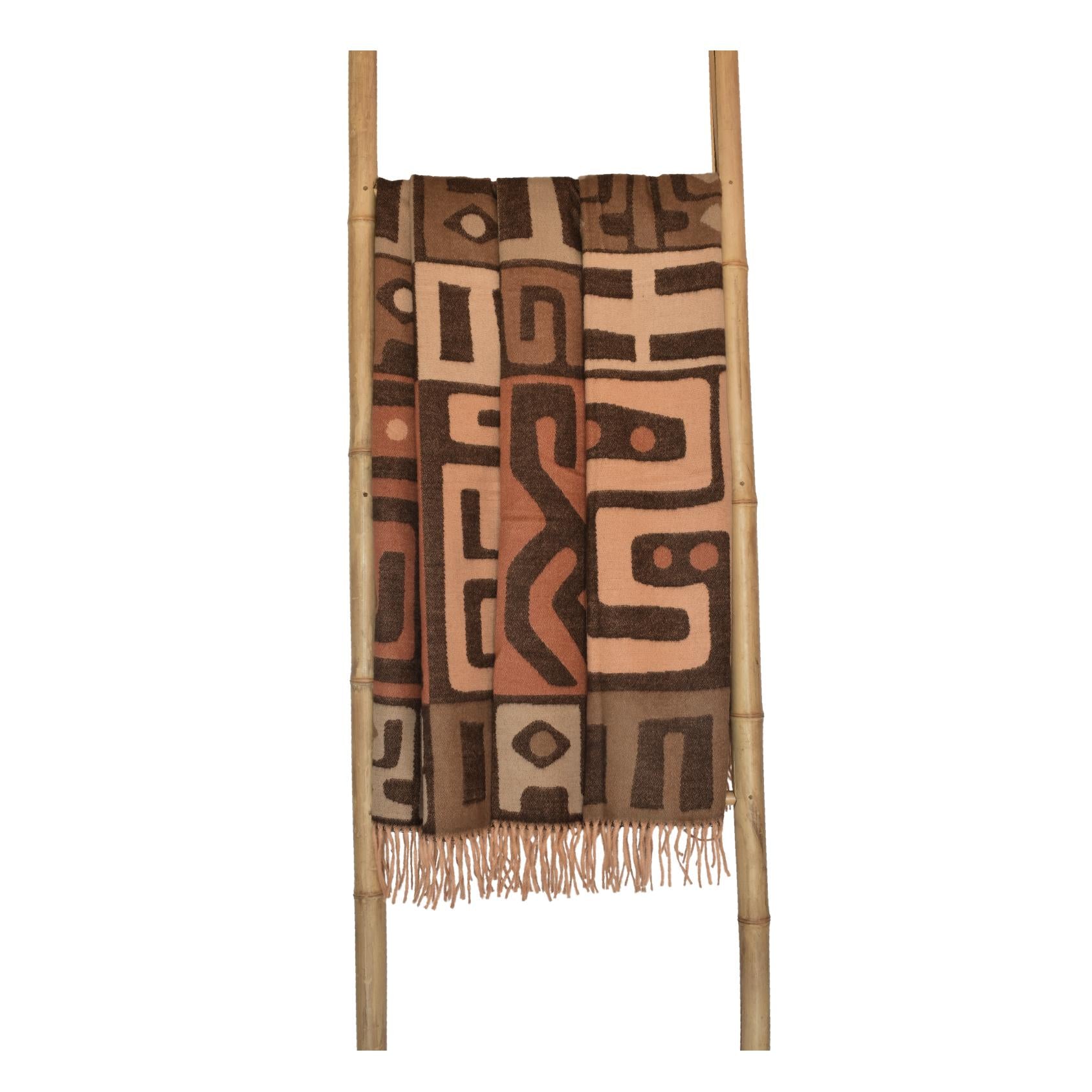 Patterned kuba cinnabar and clay throw blanket draped over a wooden ladder