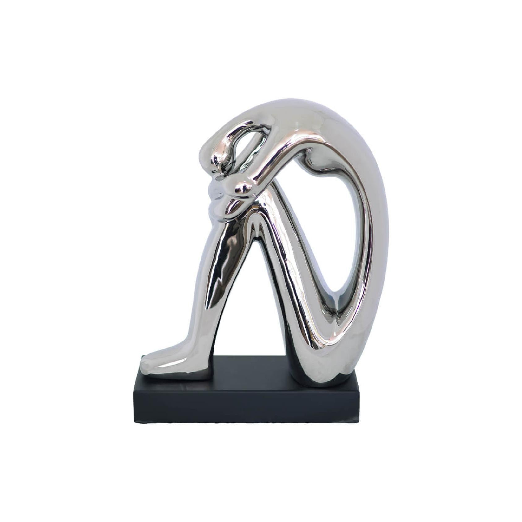Abstract sculpture of a seated figure with a reflective silver metallic finish, mounted on a rectangular black base