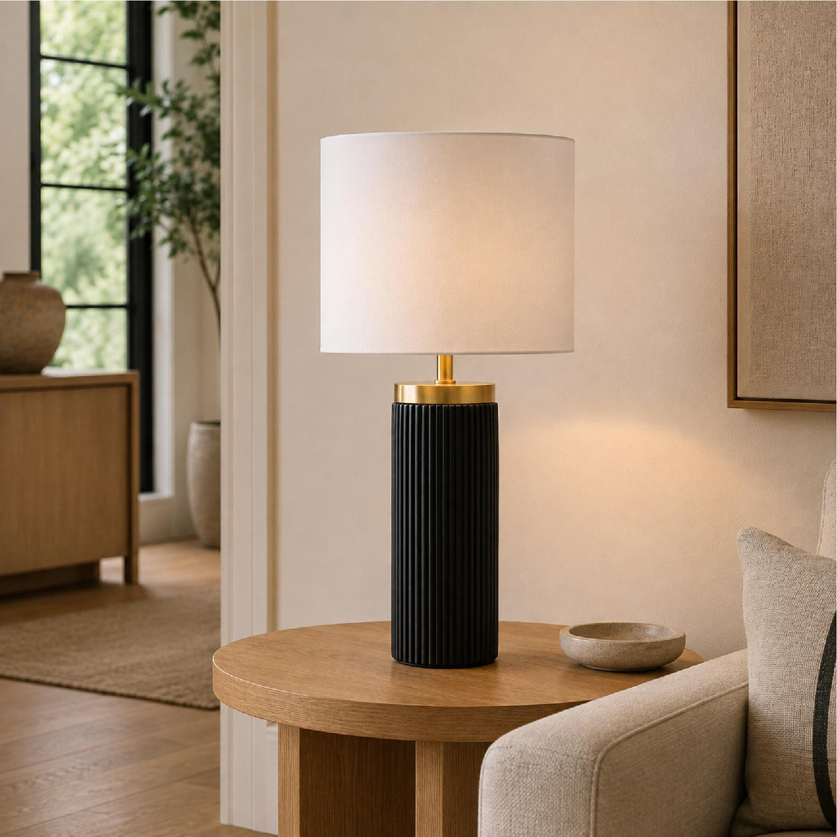 A modern table lamp with a black ribbed cylindrical base and a white shade, on a round wooden side table