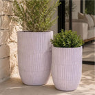 Two tall, ribbed grey ceramic planter pot with plants on a patio