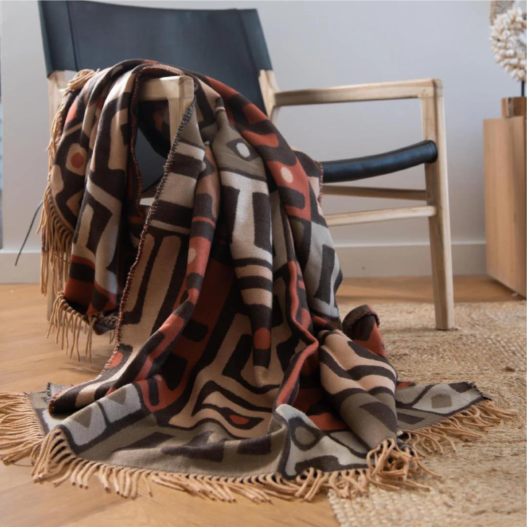Patterned kuba cinnabar and clay throw blanket draped over a chair