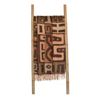 Patterned kuba cinnabar and clay throw blanket draped over a wooden ladder