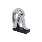 Abstract sculpture of a seated figure with a reflective silver metallic finish, mounted on a rectangular black base