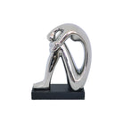 Abstract sculpture of a seated figure with a reflective silver metallic finish, mounted on a rectangular black base